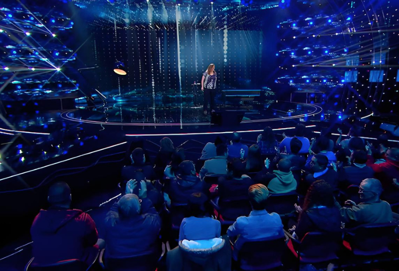 Sylvia Langford en el escenario durante una presentación con un fondo de luces y público